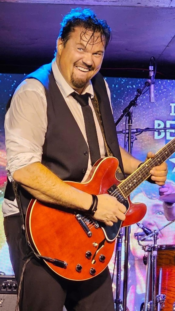 Håvard Pedersen live on stage with electric guitar under red stage lights